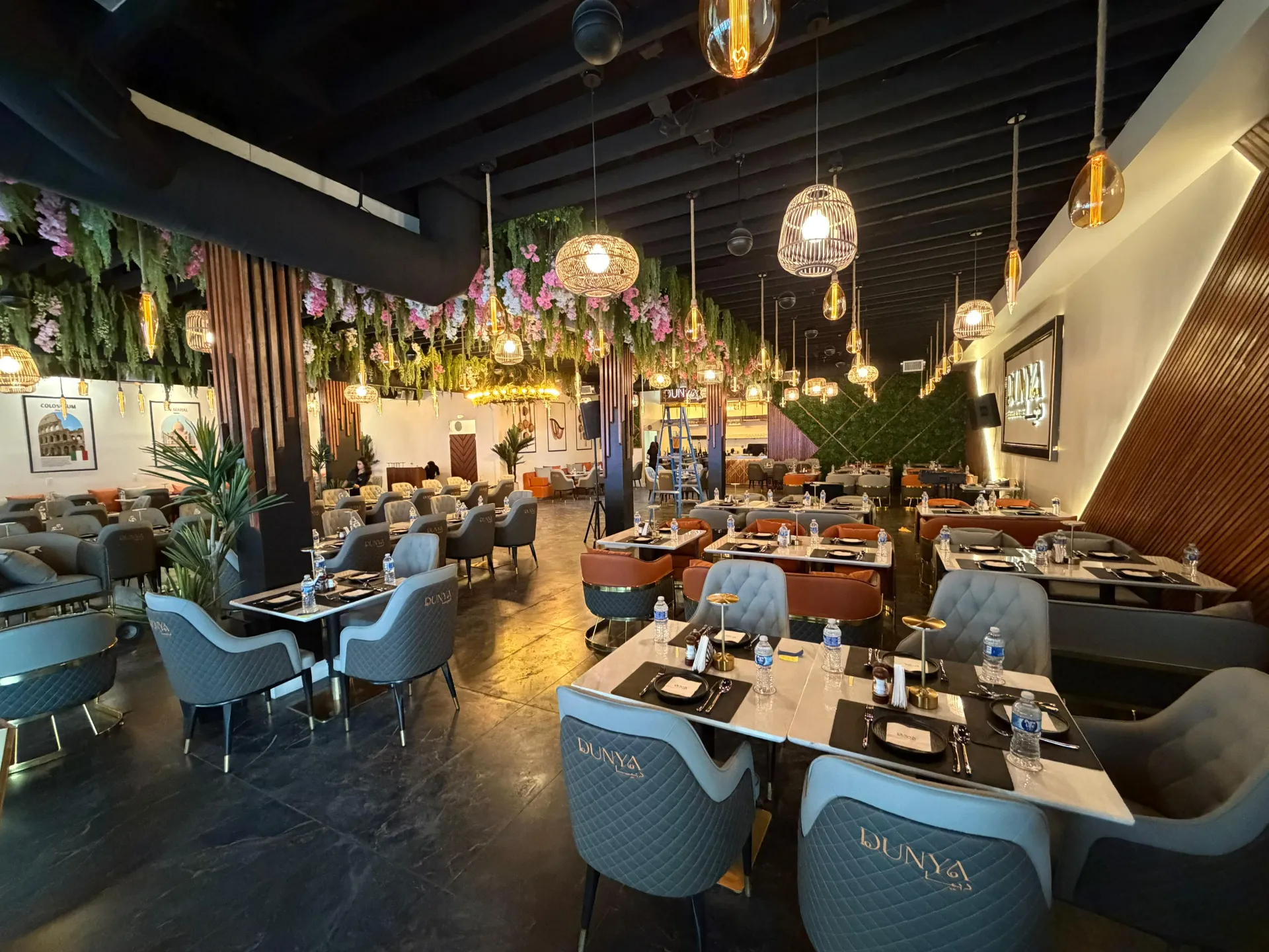 DUNYA dining hall with tufted branded chairs, marble tables, pendant lighting, floral ceiling details, and guests seated for the evening
