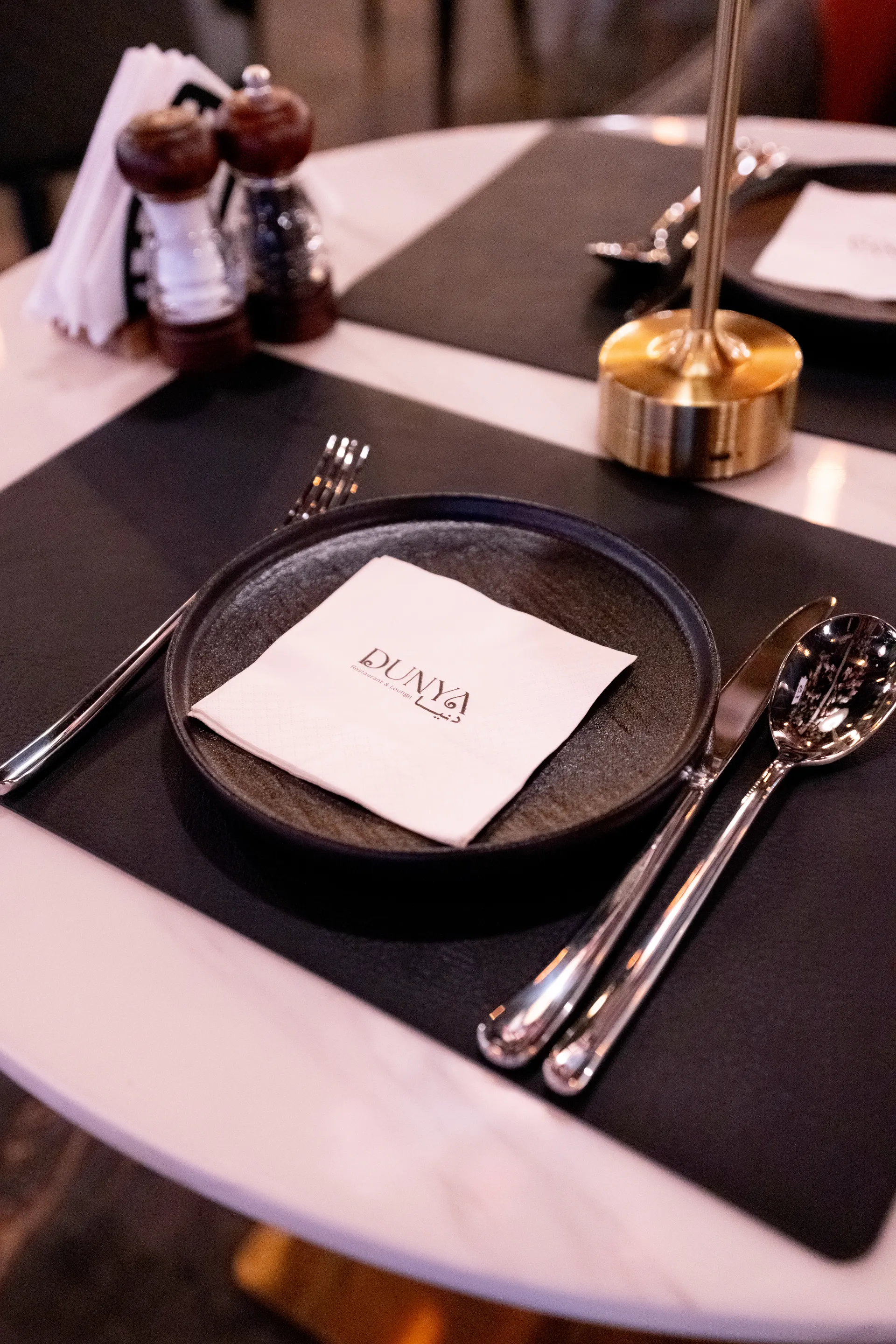 DUNYA marble table set with a branded napkin, brass lamp, mills, plate, and polished cutlery